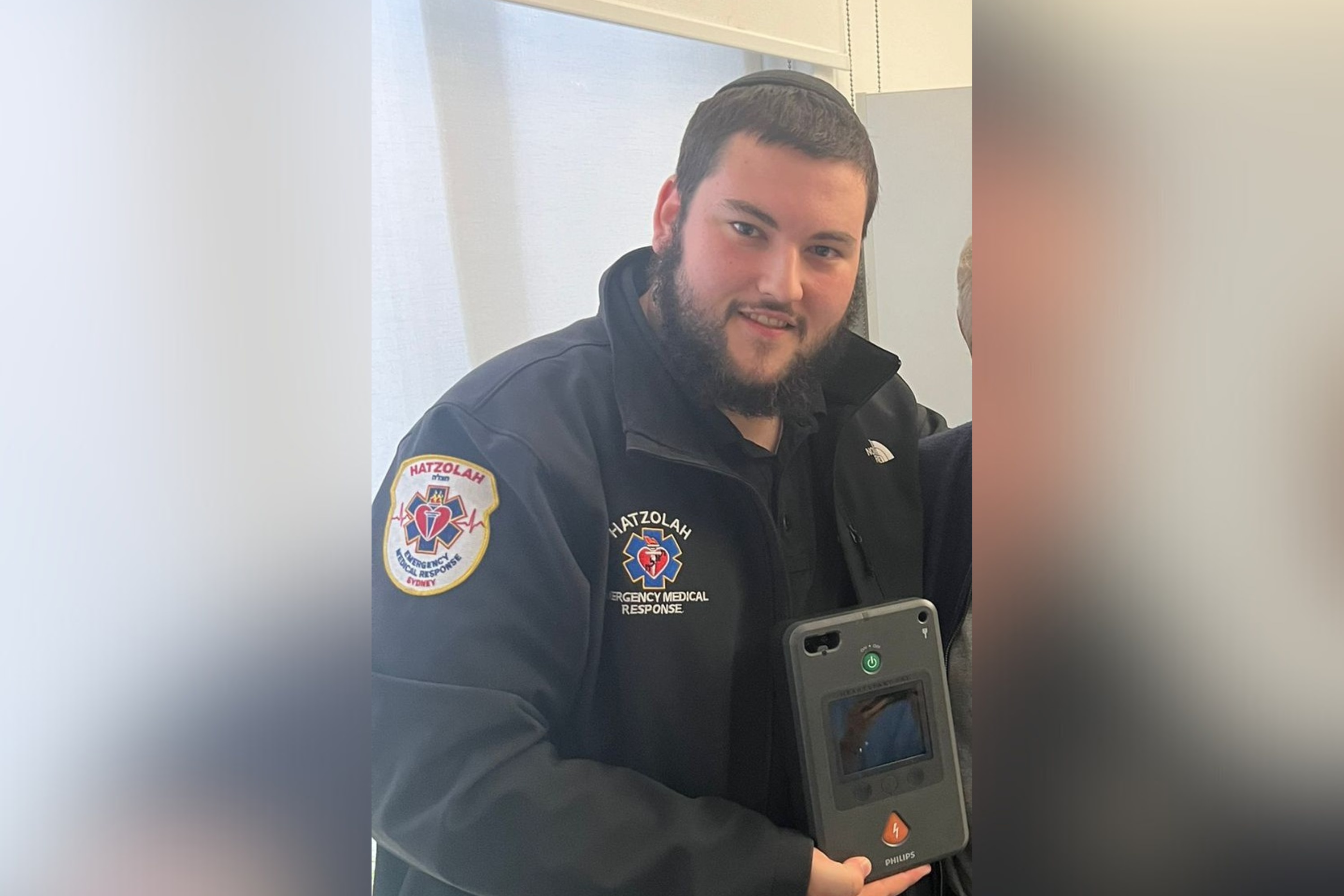 Yaakov Super holding a tablet, wearing a medical volunteer uniform.