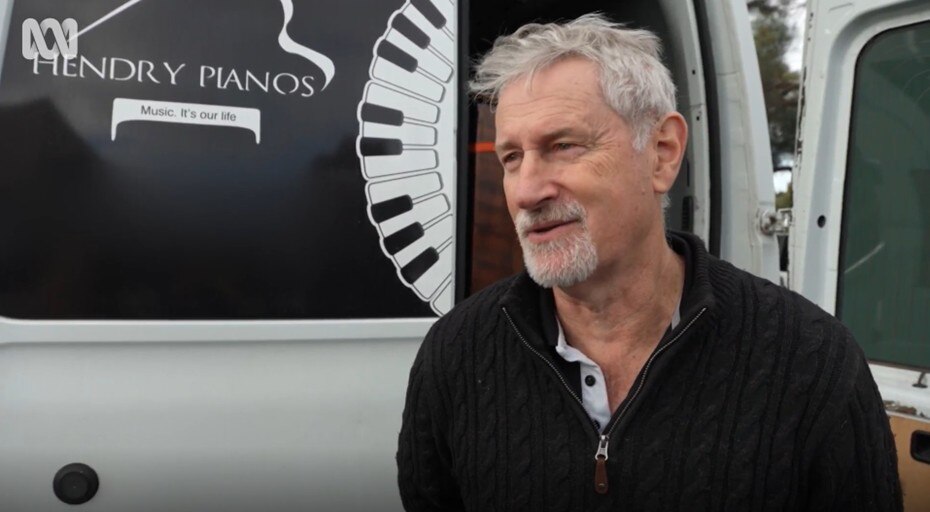 Mike Hendry, in a black sweater, standing in front of his Pianos Recycled piano-moving van.