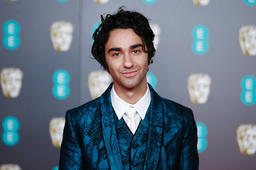 Alex Wolff wearing a dark blue suits with a matching vest.