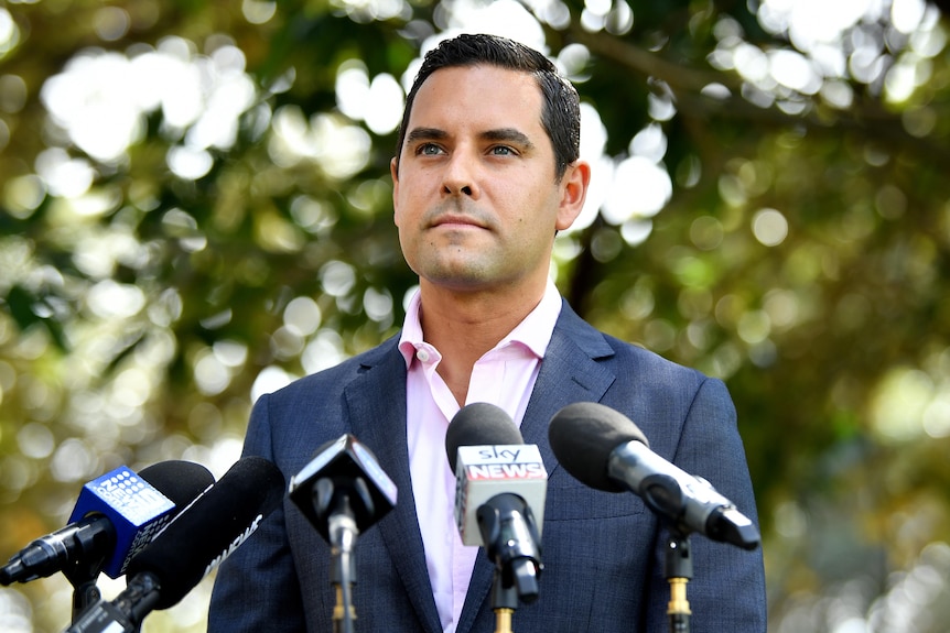 A young man standing outdoors behind microphones and talking to the media.