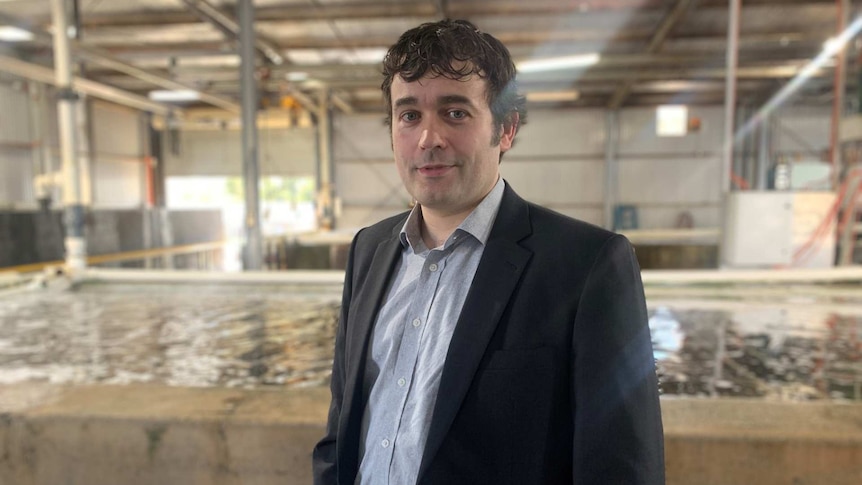 Man in suit standing in front of abalone tank.