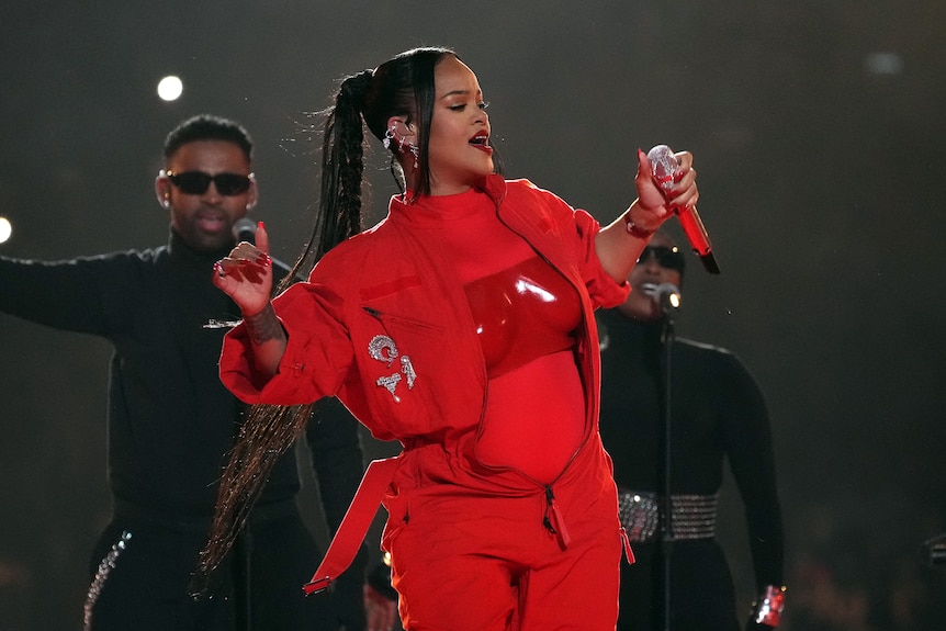 Rihanna holds up her arms as she performs on stage in front of backup singers
