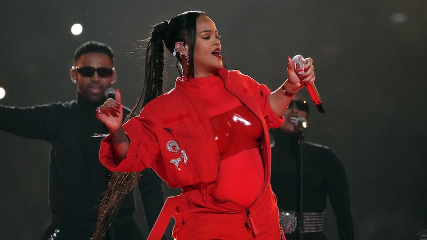 Rihanna holds up her arms as she performs on stage in front of backup singers