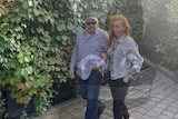Man in grey shirt and cap walks alongside red-haired woman 