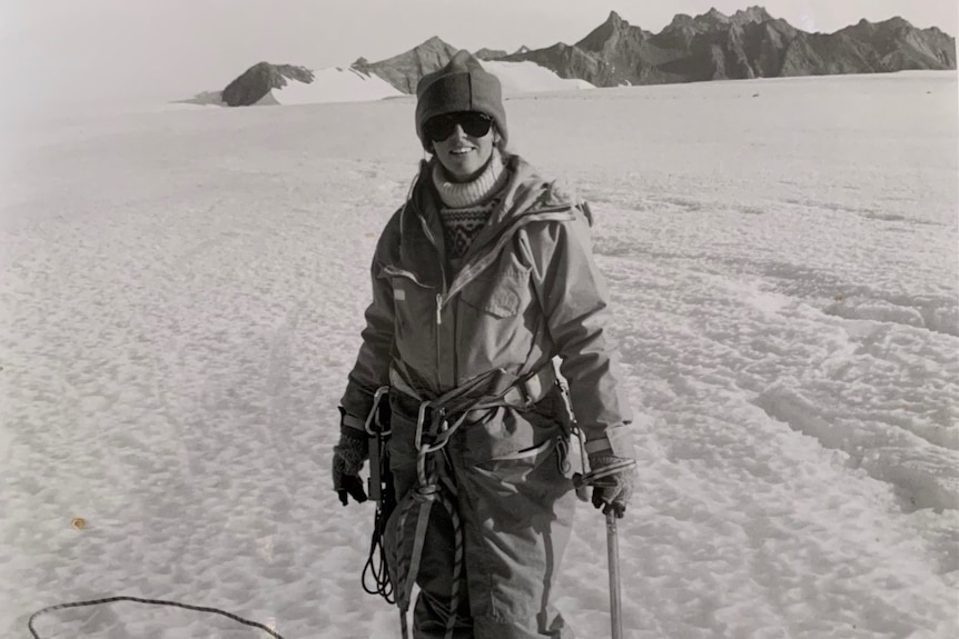 a black and white photo of a woman in the snow, with spikes on her shoes and she is wesring snow gear