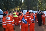 A group of State Emergency Service volunteers stand wearing orange hi-vis clothing near cars and bushland.