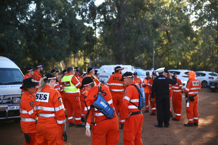 A group of State Emergency Service volunteers stand wearing orange hi-vis clothing near cars and bushland.