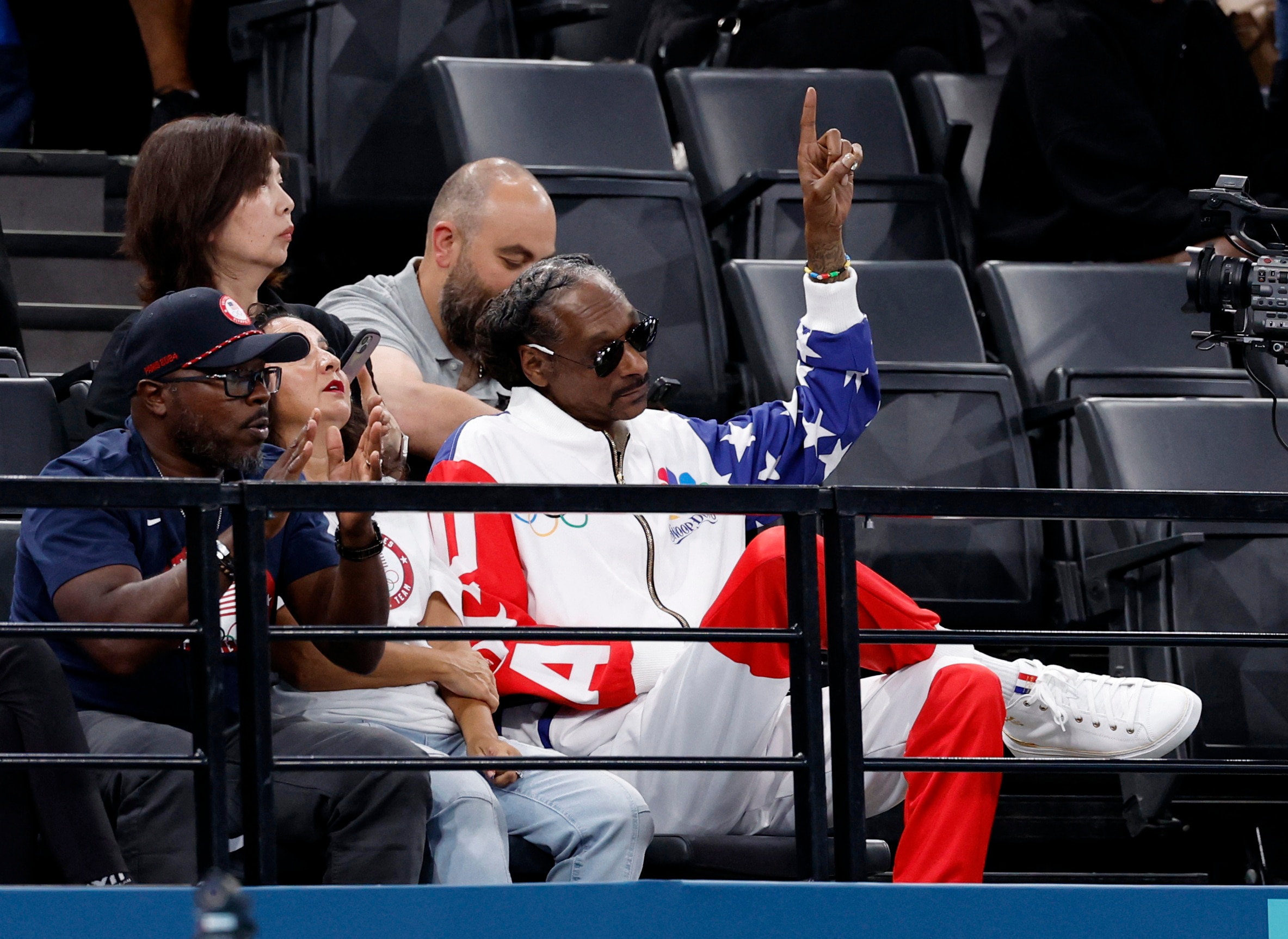 Snoop Dogg in an american flag tracksuit and sunglasses pointing his finger in the air. 