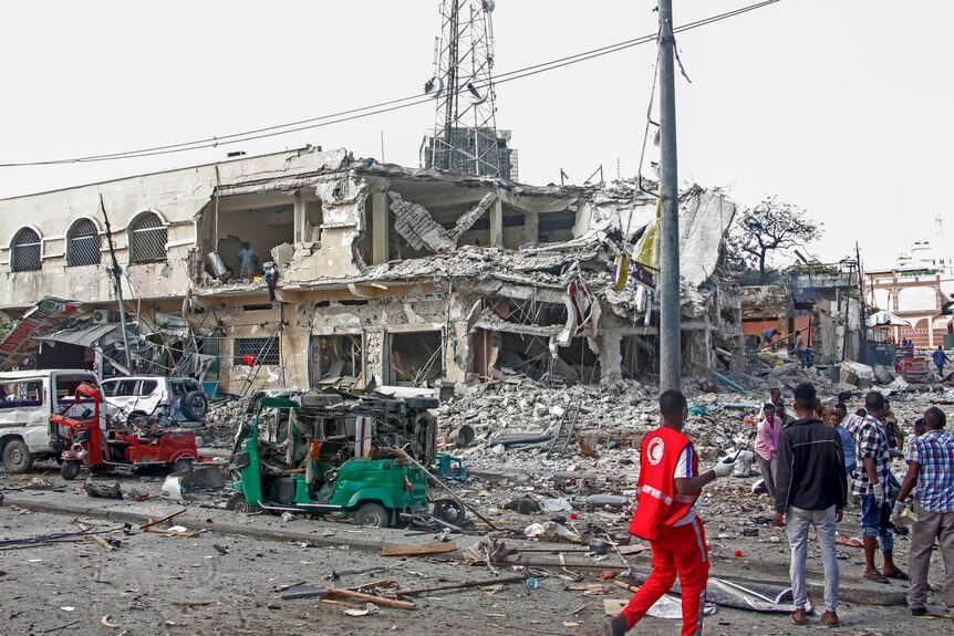 People observe a destroyed building and vehicles at the scene of a two car bombs attack.