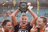 Ali Brigginshaw lifts the NRL trophy in the rain, with Brisbane Broncos teammates on either side of her.