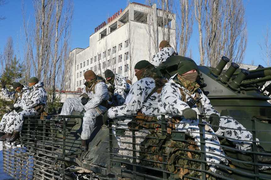 Ukrainian troops in snow camouflage sit on an armoured vehicle in front of an old Soviet-era building. 