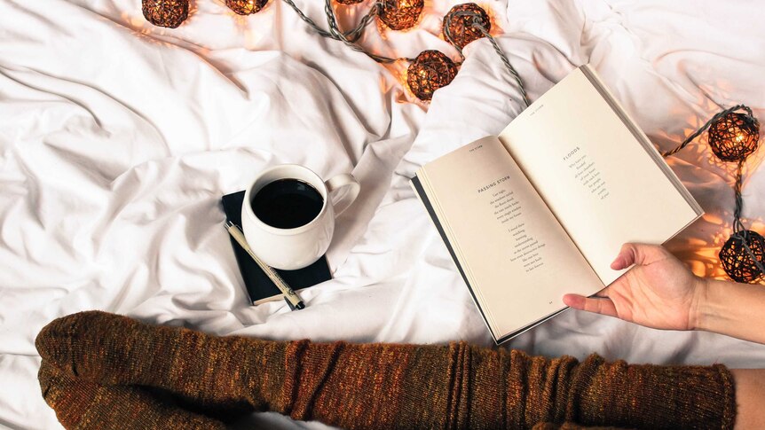 Woman sits on bed with coffee reading a book to depict words that bring people comfort.