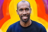 A photo of a man smiling to camera against a colourful illustrated background.