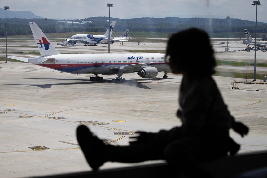 A silhouette of a little girl in front of a window looking at the tarmac with Malaysia airlines planes. 