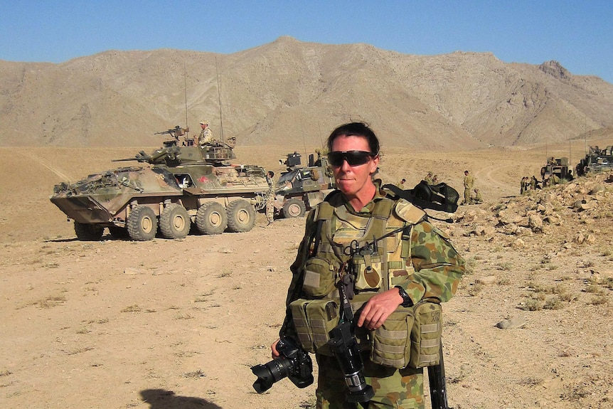 Cpl Rachel Ingram standing in front of military vehicles in a barren mountainous landscape in Afghanistan in 2009