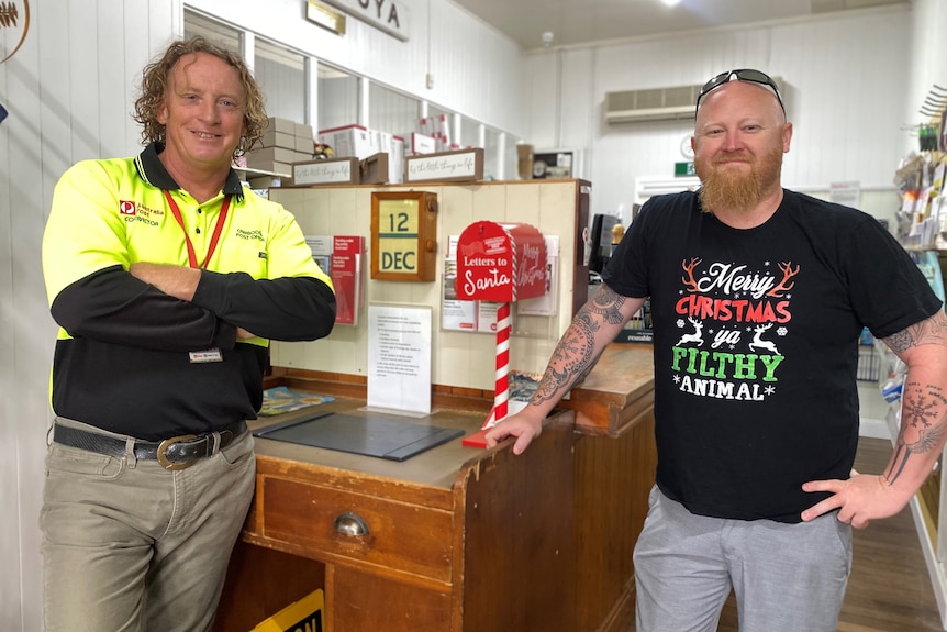 Two men smile next to a post box marked Letters for Santa.