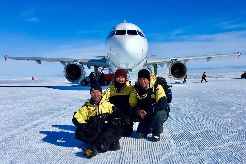 Pete, Fiona and Mark crouch in front of a jet plane, on a snowy runway.