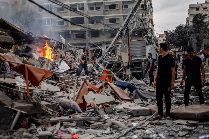 People are watching a fire burn on top of the rubble of a residential building in Gaza.