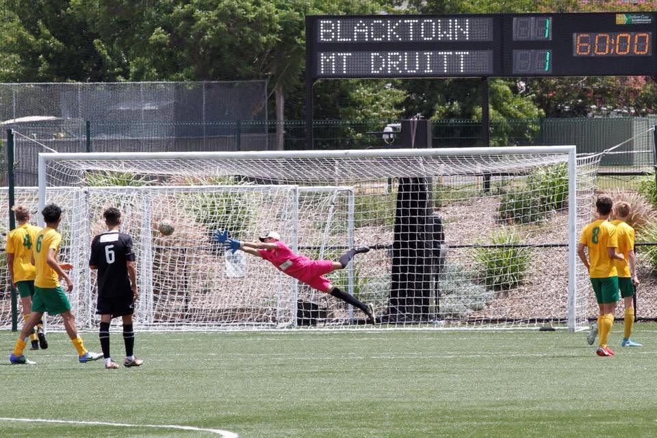 Beach in a full stretch trying to stop a soccer ball from going into the goal.