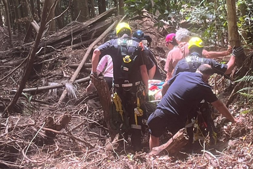 Rescuers carrying a woman through bush.