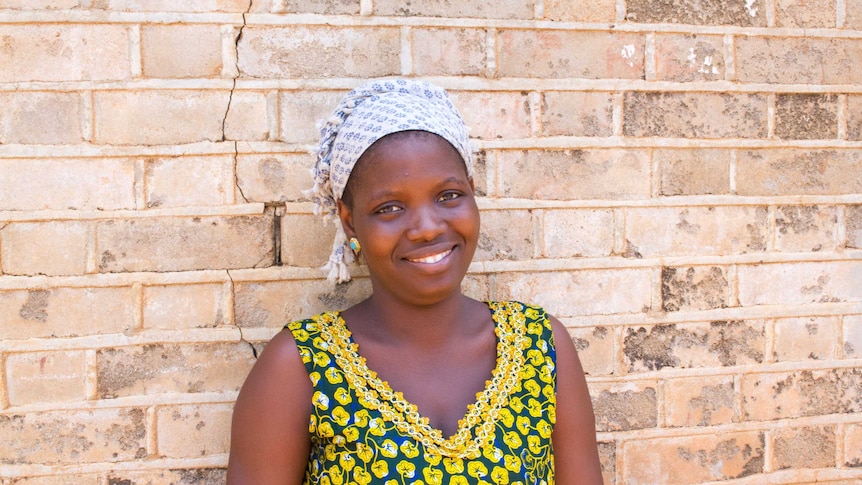 Mariama standing in front of a brick wall smiling.
