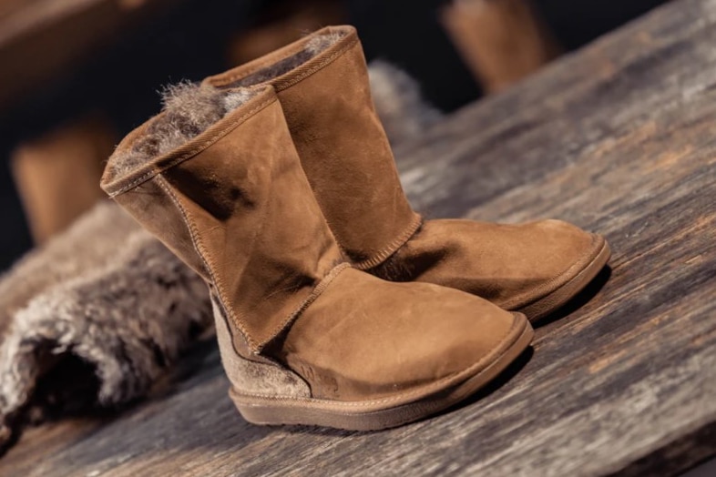 A pair of brown ugg-boot like boots on a rustic wooden surface.