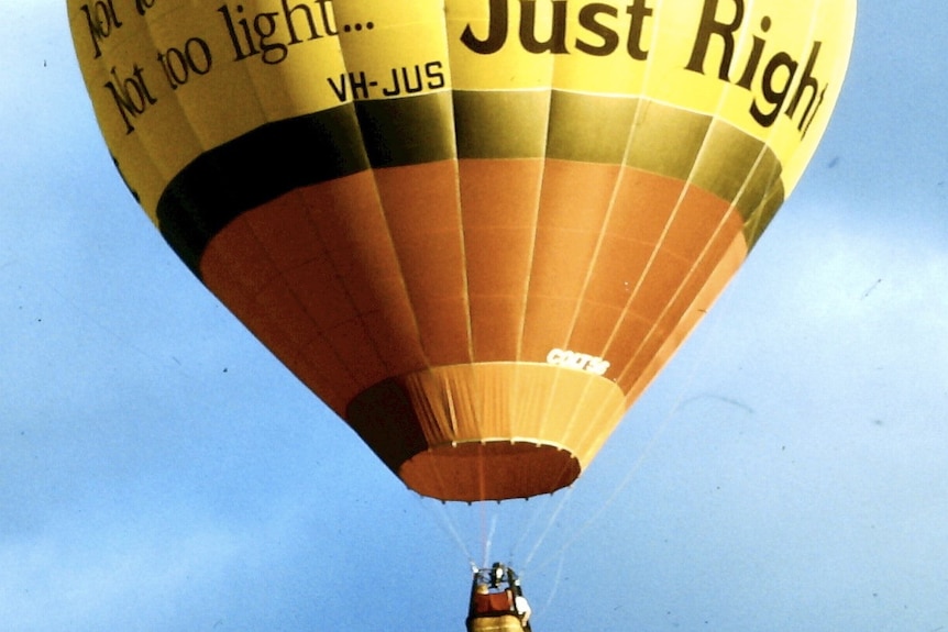 A large yellow hot air balloon with stripes of orange and the Kellogg's logo floats high in the blue sky.