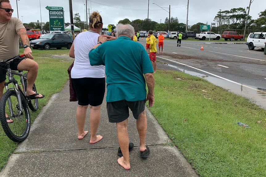 Elderly man leans on woman's shoulder tries to put shoes on after being rescued from floods 
