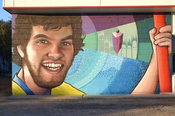 A brightly coloured mural of a bearded man in his twenties smiling