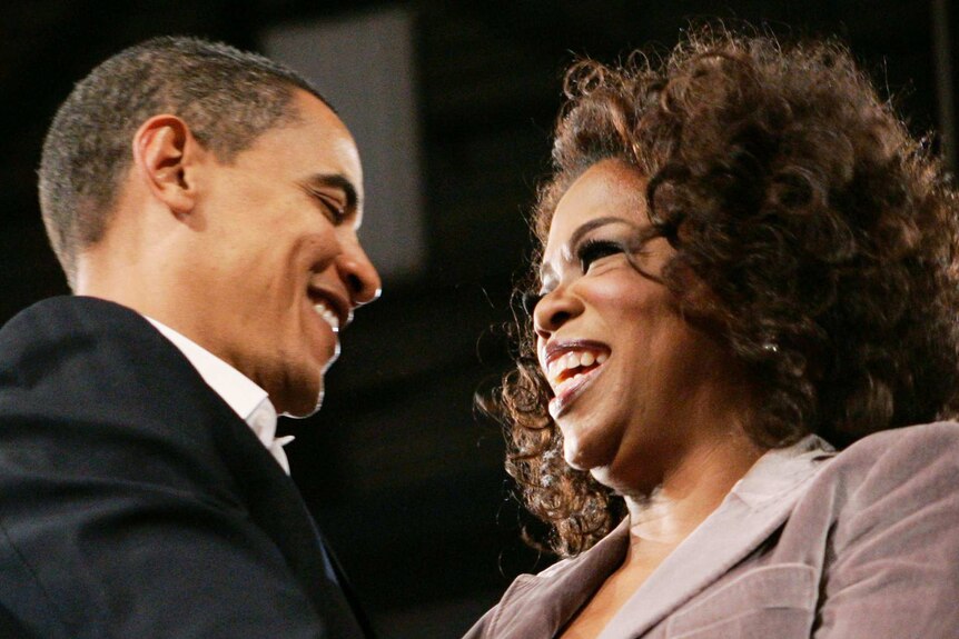 Barack Obama on the left of shot embraces Oprah Winfrey on the right, both smiling