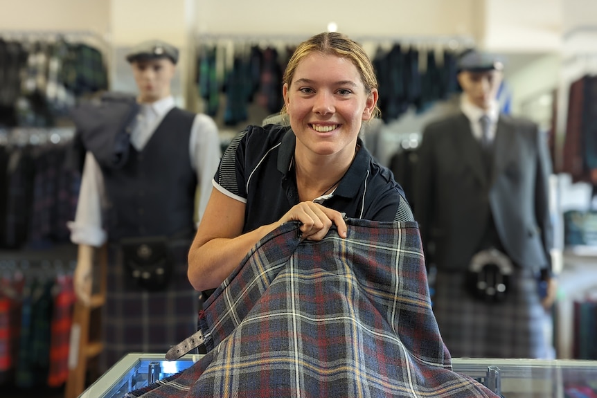 A woman smiles as she holds a bolt of tartan.