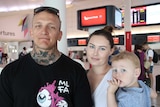 A man and a woman stand posing for a photo holding a little boy in Perth Airport.