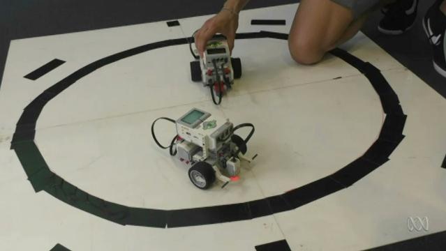 Hands hold small vehicle robots on floor inside big black circle