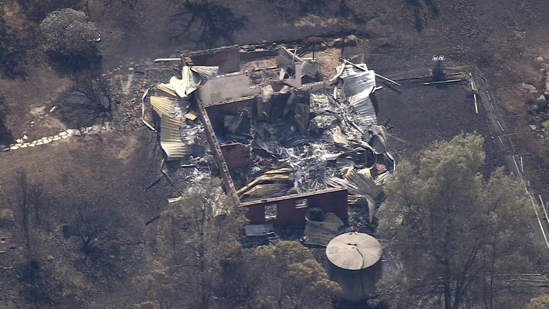 Um edifício devastado por um incêndio está cercado por grama e árvores enegrecidas.