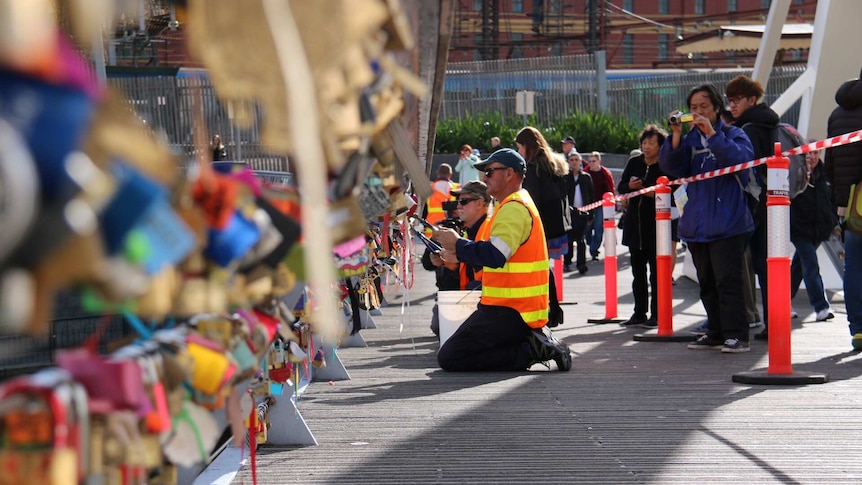 Tourists look in as Melbourne City Council workers set about removing padlocks from Southgate footbridge.