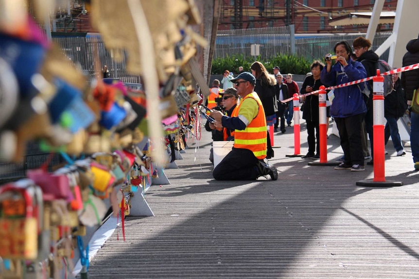 Tourists look in as Melbourne City Council workers set about removing padlocks from Southgate footbridge.