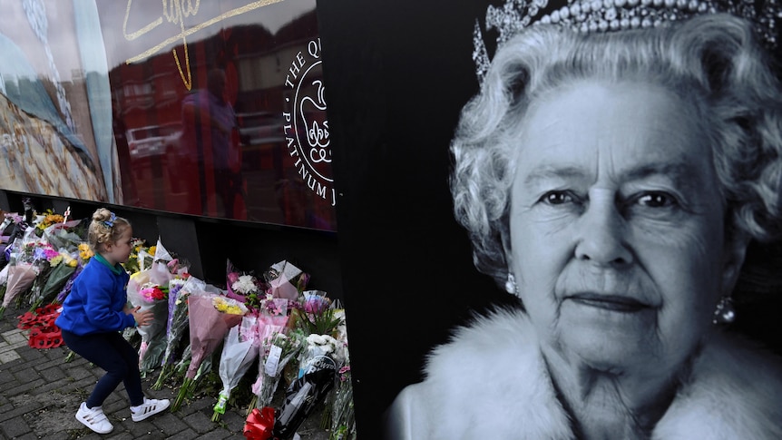 A child leaves a bouquet of flowers near a pile of others at a memorial for Britain's Queen Elizabeth.