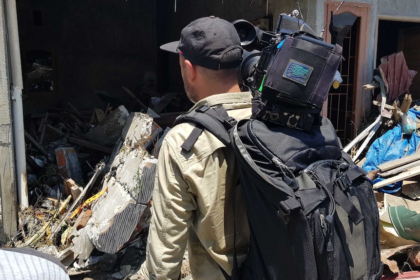 Back of cameraman with camera on shoulder looking at damaged building.