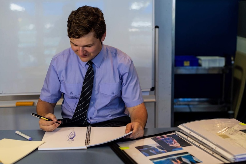 Aspiring fashion designer Connor O'Grady, dressed in his school uniform, sketches in a book.