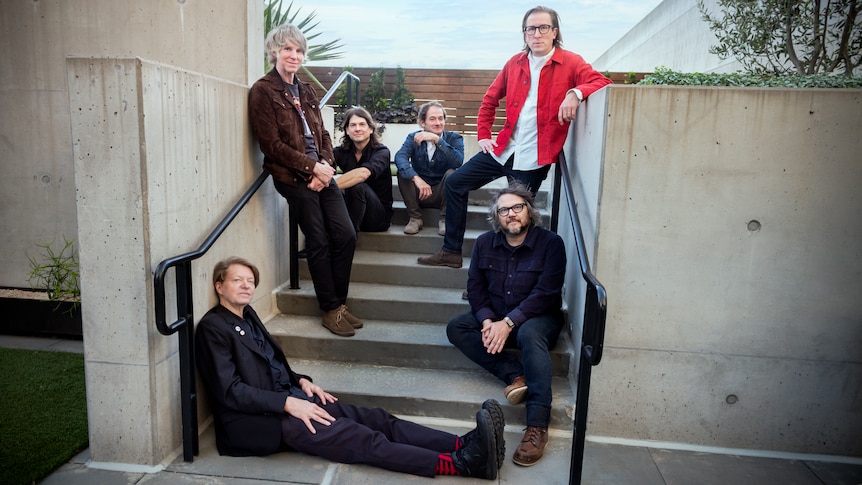 The six members of Wilco pose on a concrete stairwell outside