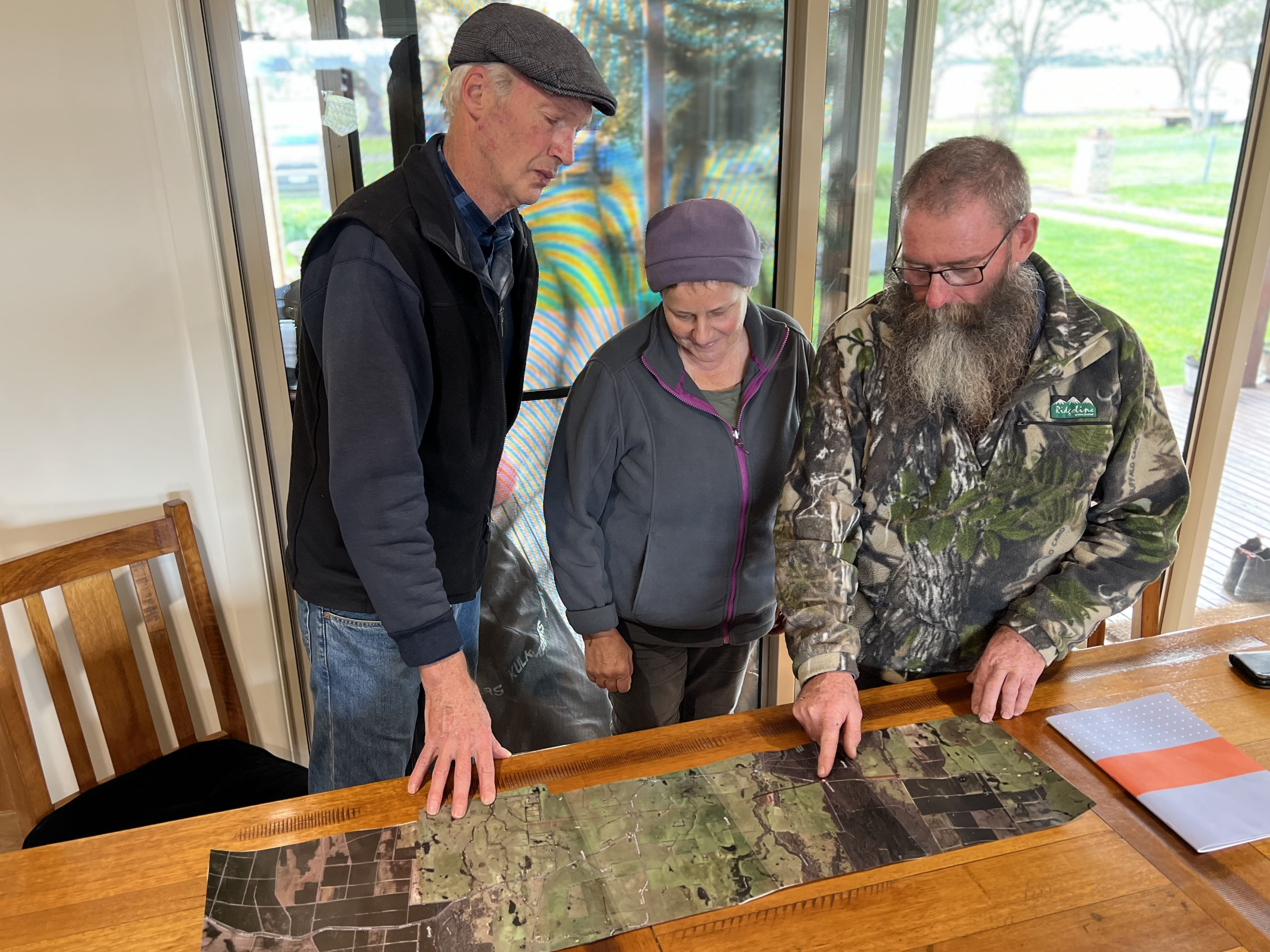 Three farmers stand looking at a map on a kitchen table