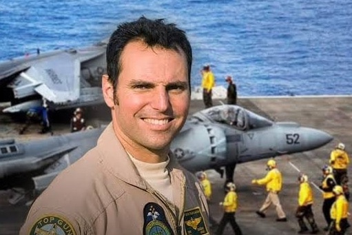 Man in airforce uniform with planes on a ship behind him. 