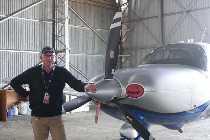 A man standing next to the propeller of a light airplane
