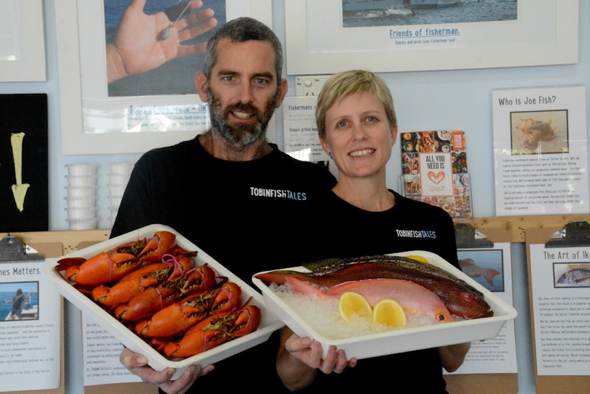 A man and a lady holding two trays of seafood in a fish and chip shop