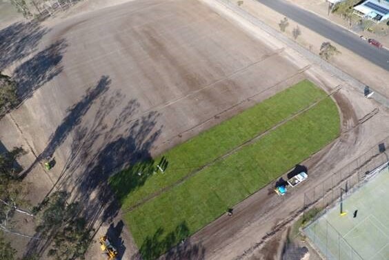 An aerial shot of brown school yard with strips of green turn starting to be laid at one end.