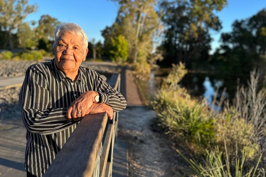 Lorraine Peeters leans against a railing near a river and looks toward the camera in a striped shirt