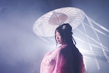 A dramatically lit portrait shows a woman in back-lit in a smoky room wearing traditional Chinese clothing.