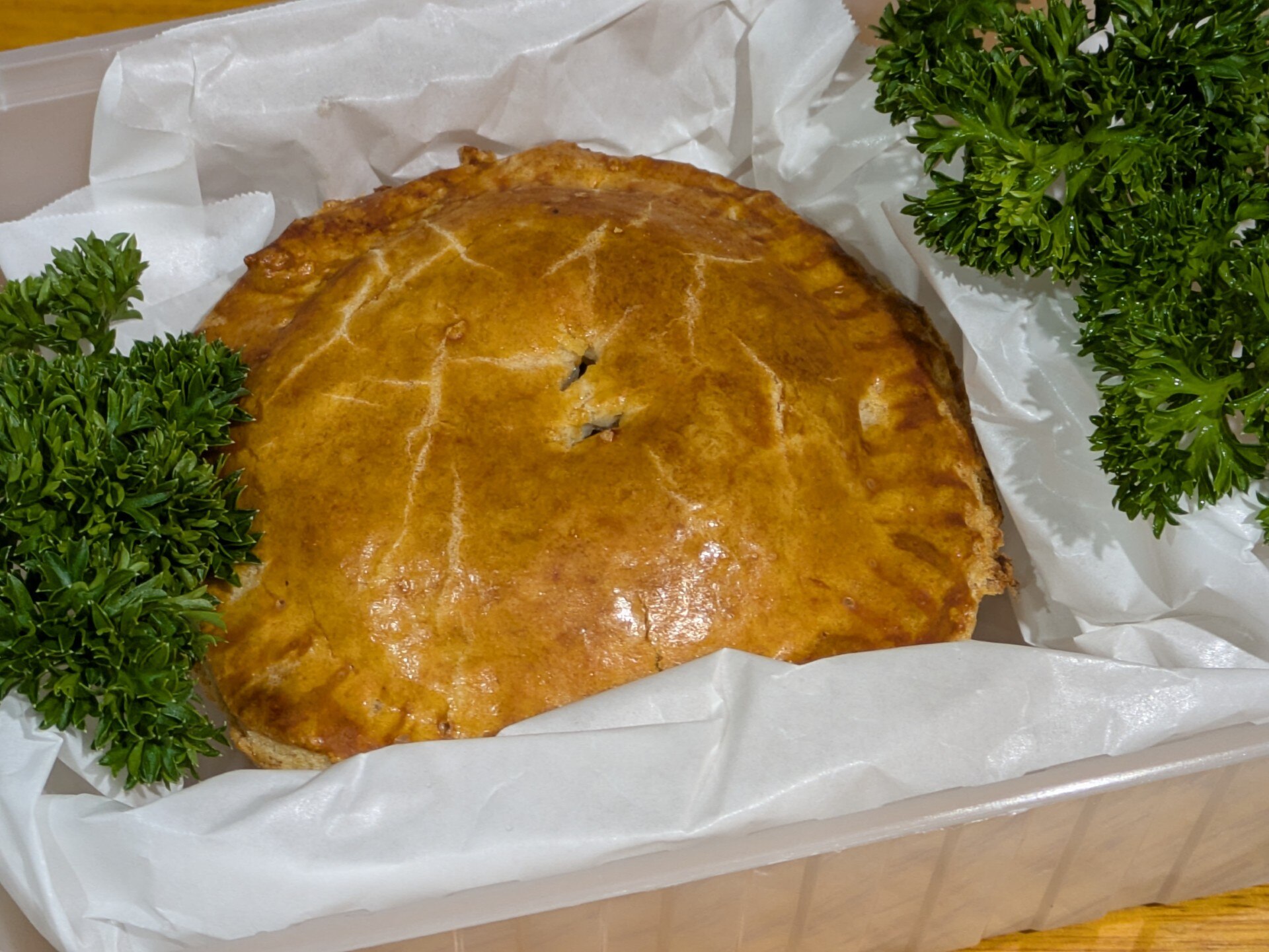 Steak and kidney pie in a tray with baking paper and garnish 