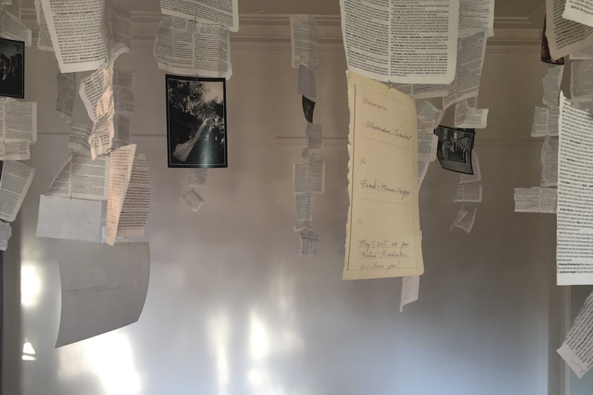 An installation by Lexi Eikelboom, pages of a bible and photos hanging by wire from a ceiling inside her Melbourne home