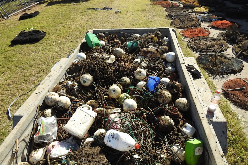 A skip bin filled with line and floats with more pots on the ground.